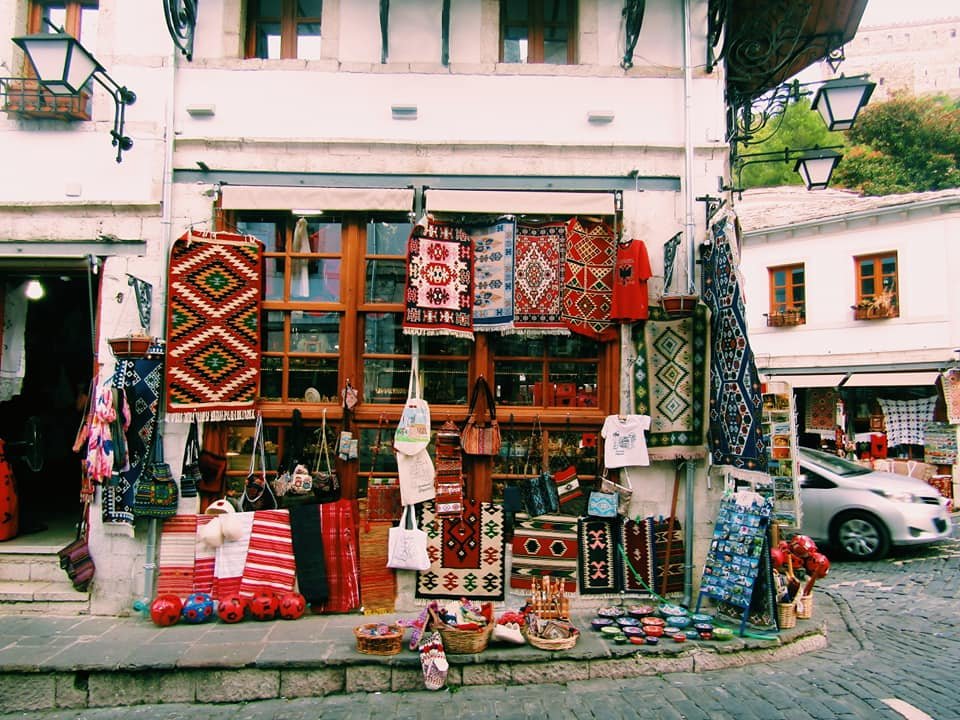 a shop on the corner of a cobbled street in Gjirokaster selling handwoven rugs and traditional Albanian clothing and souvenirs
