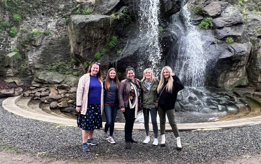 a group of 5 friends standing in front of a small waterfall