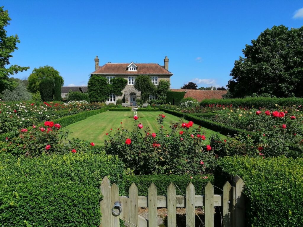 a large english manor house with a manicured garden and red flowers