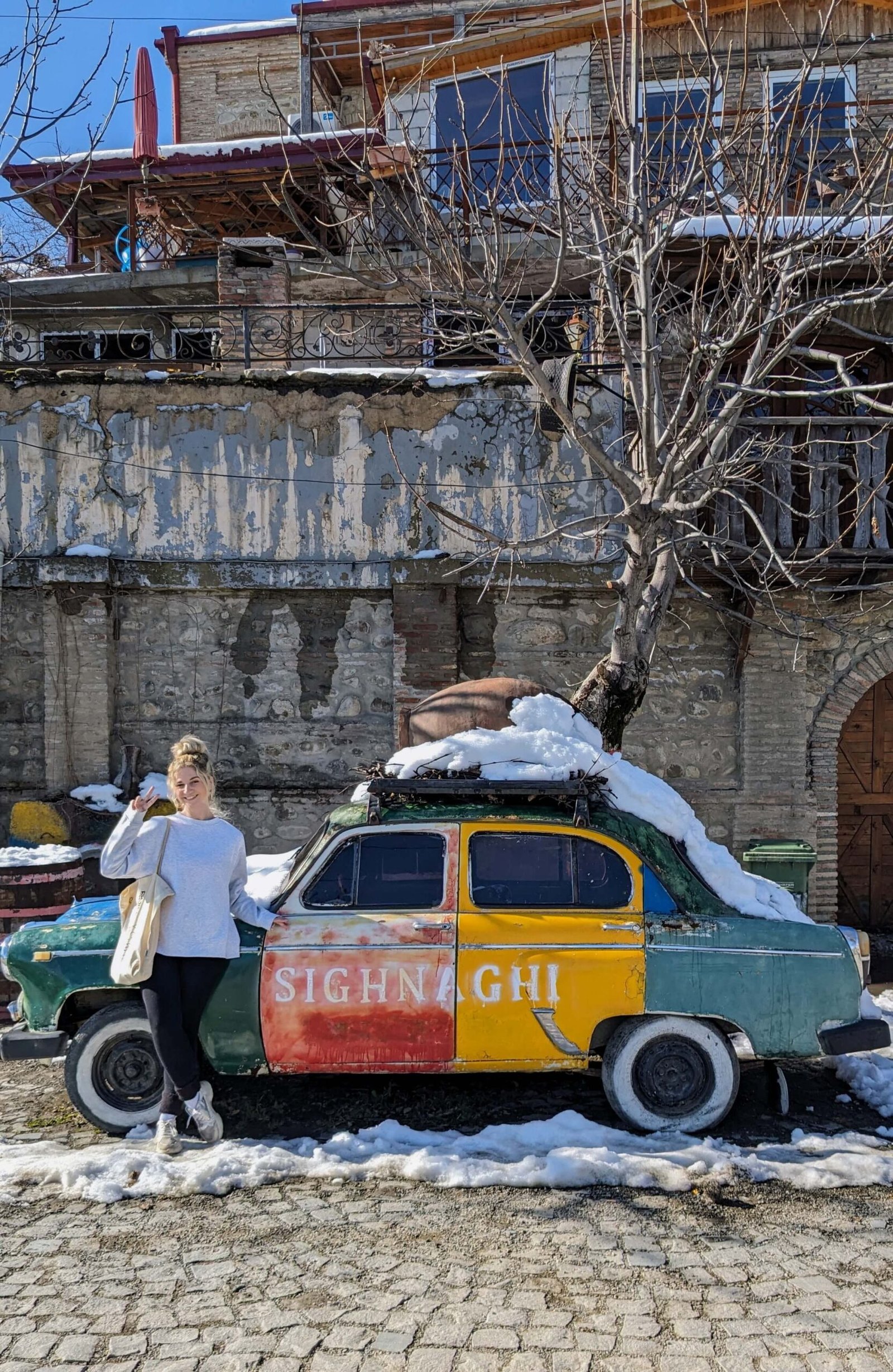the author poses next to a multicoloured car in sighnaghi
